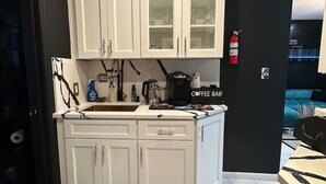Una cocina moderna con gabinetes blancos, un felpudo con estampado de mármol y una barra para café.