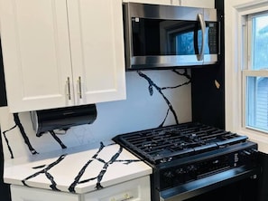 A kitchen with white cabinets, a black stove, and a stainless steel microwave.
