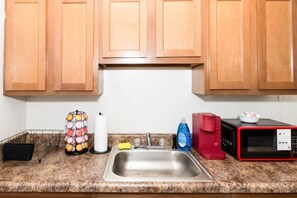 A kitchen with wooden cabinets, a stainless steel sink, a red coffee maker, a black microwave, and a dish rack with dishes. - 610b Large One Bedroom Downtown! (Albany)