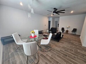A modern living room with a glass dining table, white chairs, a black sofa, and a ceiling fan. - 632 4 Large Bedrooms Spacious Private Yard (Dallas)