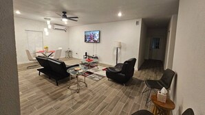 A modern living room with a flat-screen TV, black leather sofas, a glass coffee table, and a ceiling fan. - 632 4 Large Bedrooms Spacious Private Yard (Dallas)