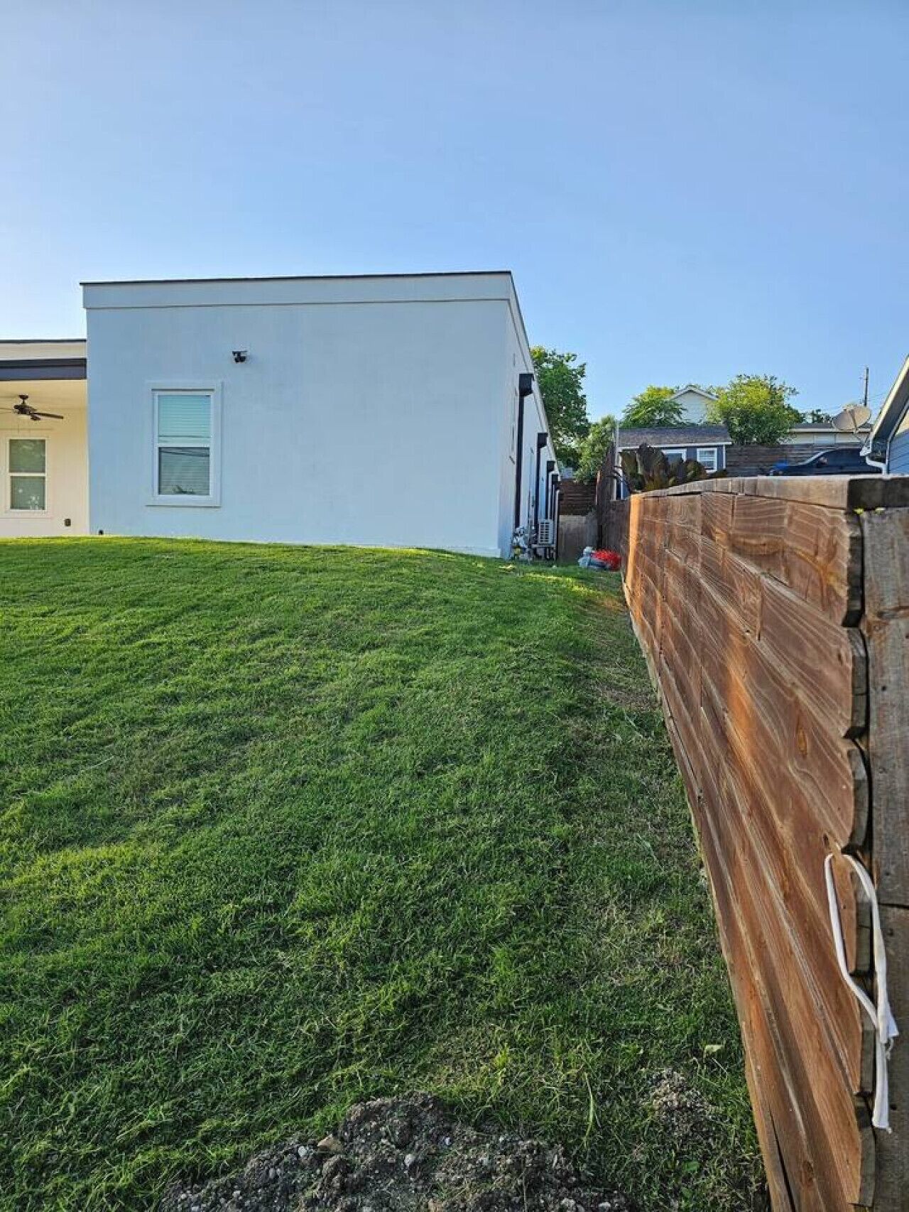 A modern white building with a flat roof, a fenced yard, and a clear sky.