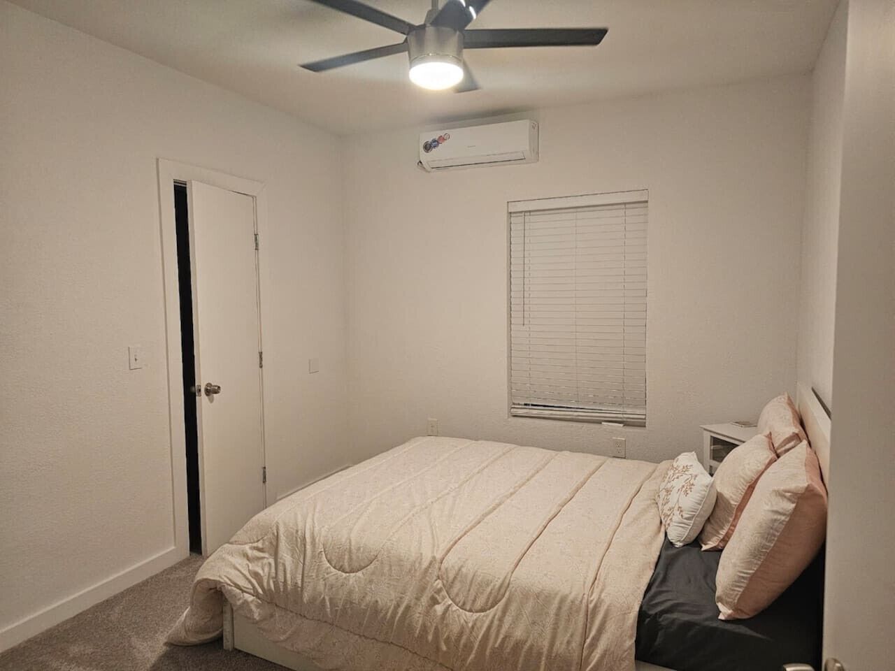 A bedroom with a bed, a ceiling fan, a window with blinds, and an air conditioning unit.