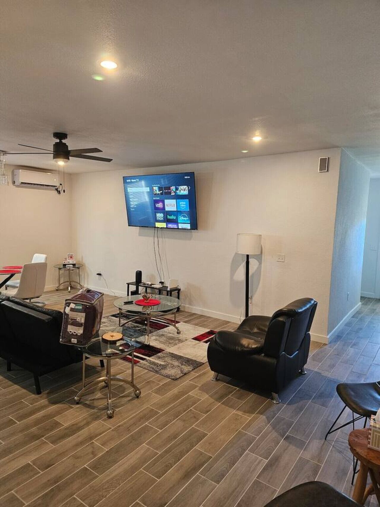 Een moderne woonkamer met een flatscreen televisie aan de muur, een plafondventilator, een salontafel, een leren bank en een klein bijzettafeltje.