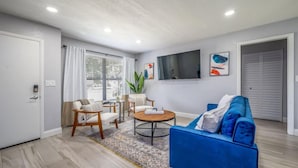 A modern living room with a blue sofa, a round coffee table, and a TV mounted on the wall. - 561j Large 2 Bedroom With King bed and Patio! (Orlando)