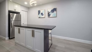 A kitchen with white cabinets, a stainless steel refrigerator, and two abstract paintings on the wall. - 561j Large 2 Bedroom With King bed and Patio! (Orlando)