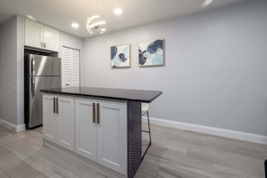A kitchen with white cabinets, a stainless steel refrigerator, and two abstract paintings on the wall.