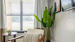 A room with a wooden chair, a small table, a potted plant, and a window with blinds. - 561j Large 2 Bedroom With King bed and Patio! (Orlando)