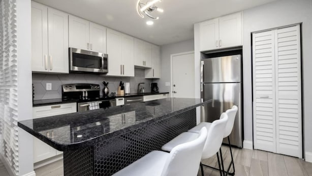 A modern kitchen with white cabinets, stainless steel appliances, a black marble island, and white bar stools. - 561j Large 2 Bedroom With King bed and Patio! (Orlando)