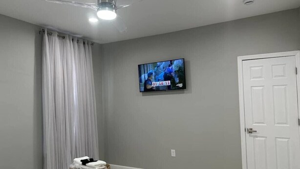 A bedroom with a bed, a television mounted on the wall, a door, and a ceiling fan. - 625 3 Large Bedrooms Luxe Artistic Art Vibe (Newark)