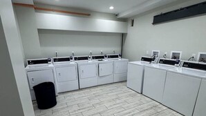 A laundry room with multiple washing machines and dryers, a trash bin, and a tiled floor. - 610e Very Comfortable Studio Downtown (Albany)