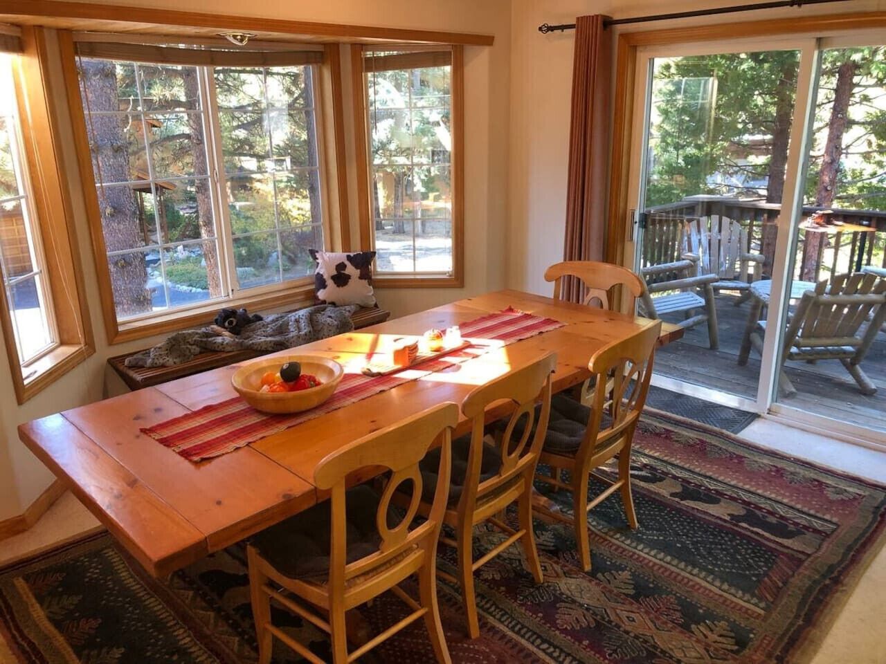 A dining area with a wooden table, four chairs, a bowl of fruit, and a stuffed animal.