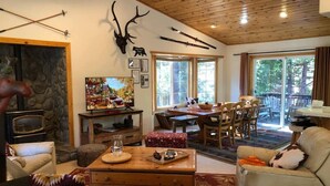 A cozy living room with a stone fireplace, wooden ceiling, and a deer head decoration. There is a dining area with a table and chairs, and a sofa with a patterned throw. - 620 Large 3 Bedrooms Outdoor Seating (Kings Beach)
