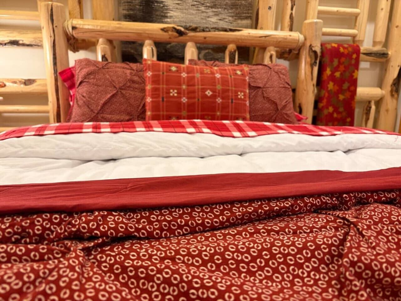 Un lit recouvert d’une couverture à carreaux rouges et blancs, d’une autre couverture à motifs rouges et de deux oreillers rouges.
