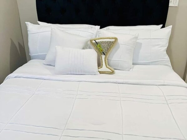 Ein ordentlich bezogenes Bett mit weißer Bettwäsche und Kissen, ein dekoratives Glasobjekt auf dem Bett und ein dunkles Kopfbrett.