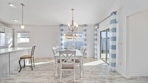 A spacious dining area with a white table and chairs, a chandelier, and a view through large windows. - 561g Massive Newly Built 3 Bedroom! (Wildwood)