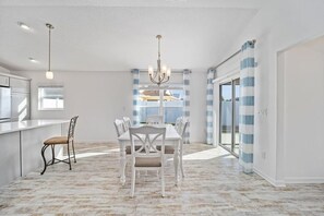 A spacious dining area with a white table and chairs, a chandelier, and a view through large windows. - 561g Massive Newly Built 3 Bedroom! (Wildwood)