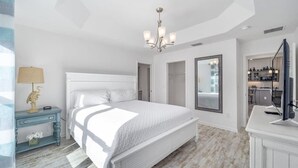 A spacious bedroom with a large bed, a chandelier, a television, and a view of the kitchen. - 561g Massive Newly Built 3 Bedroom! (Wildwood)