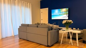 A modern living room with a grey sofa, a flat-screen TV, and a small round table with a vase of flowers. - Escape Heaven! Tranquility Guaranteed, Fully Fenced Pet Friendly (Palm Coast)