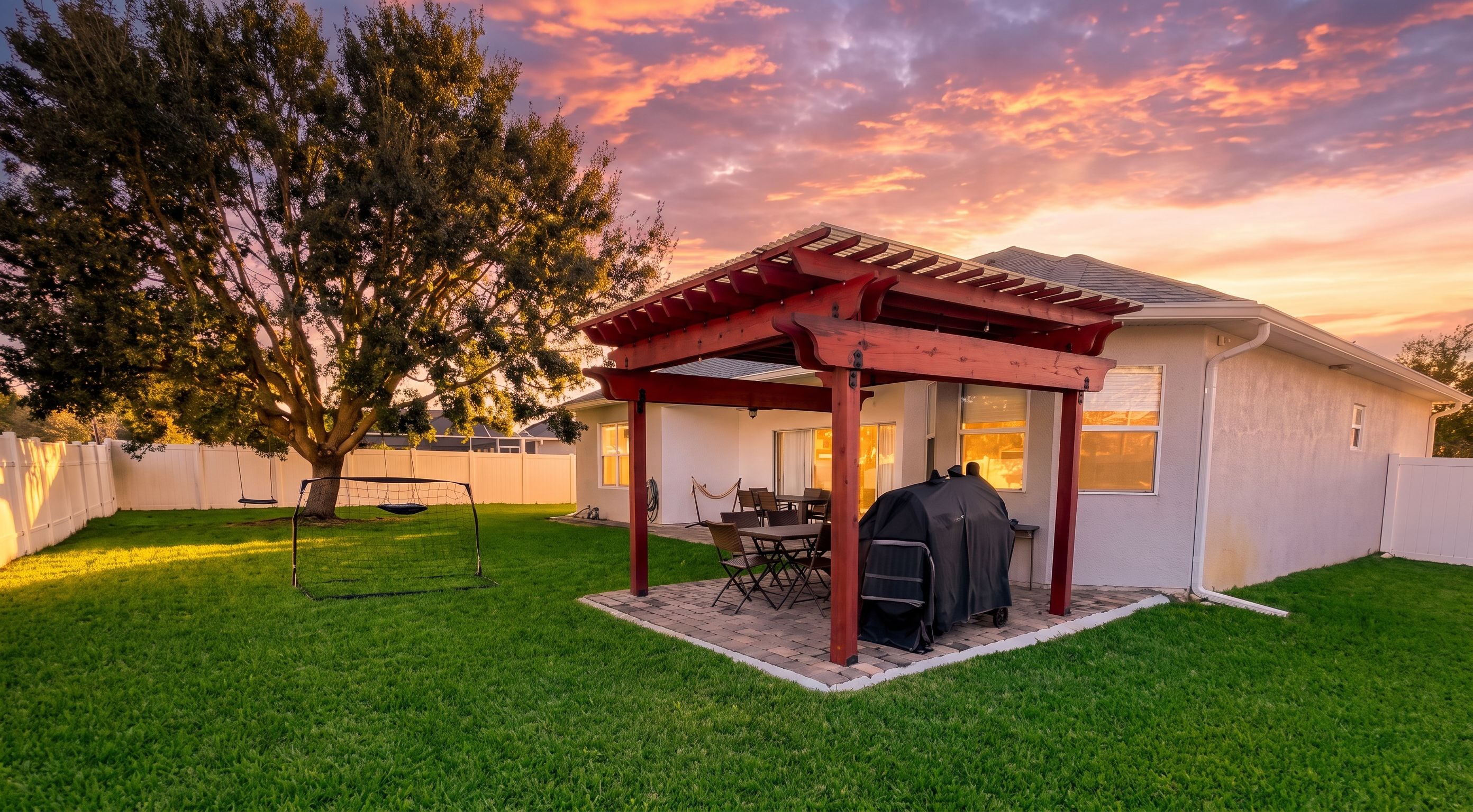 Ein Garten mit überdachter Terrasse, Schaukel und Grillplatz.