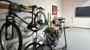 Un garaje con bicicletas y una moto, un televisor fijado a la pared y una puerta.