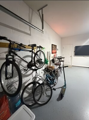 A garage with bicycles and a scooter, a TV mounted on the wall, and a door. - Escape Heaven! Tranquility Guaranteed, Fully Fenced Pet Friendly (Palm Coast)