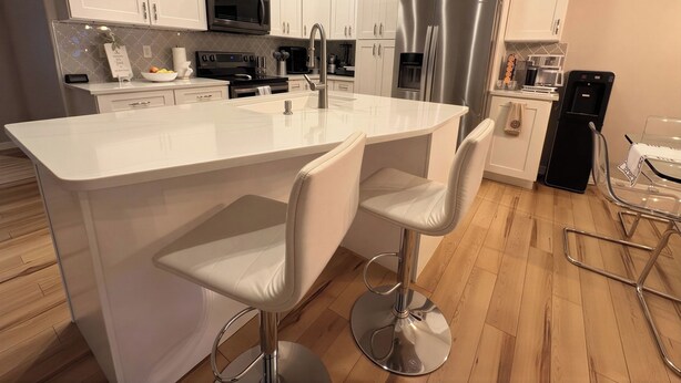 Una cocina moderna con gabinetes blancos, electrodomésticos de acero inoxidable y una isla central con taburetes de bar.