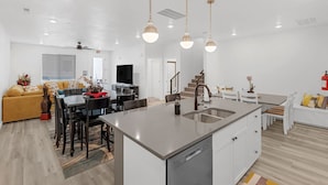 A modern kitchen with a central island, a dining area with a table and chairs, and a living room with a sofa and a TV. - 485 Rooftop Hot Tub - Sleeps 24 (Hurricane)
