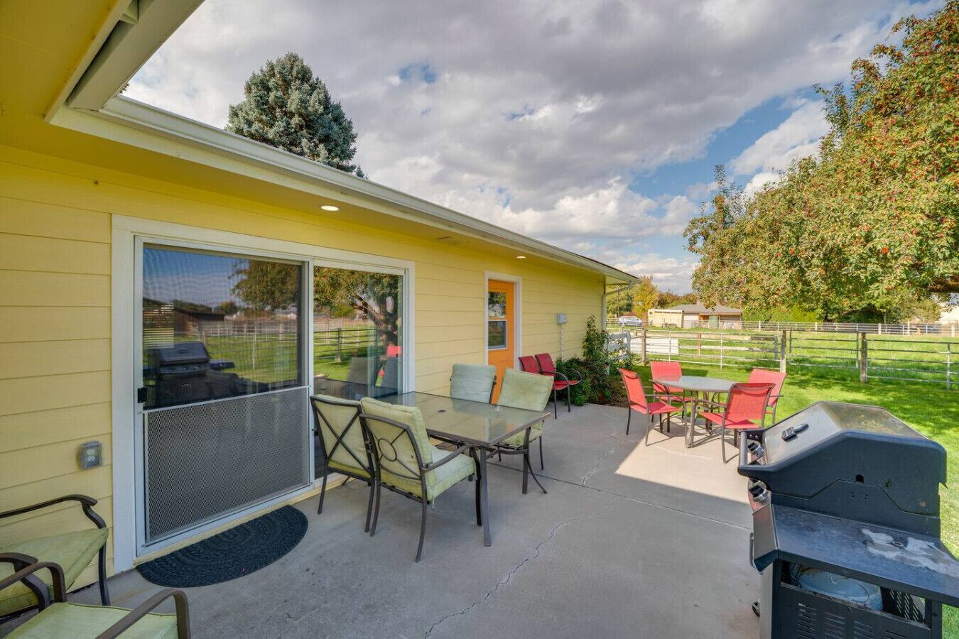 Un patio couvert avec une table et des chaises, un barbecue et une porte-fenêtre coulissante donnant sur un espace protégé par des moustiquaires.