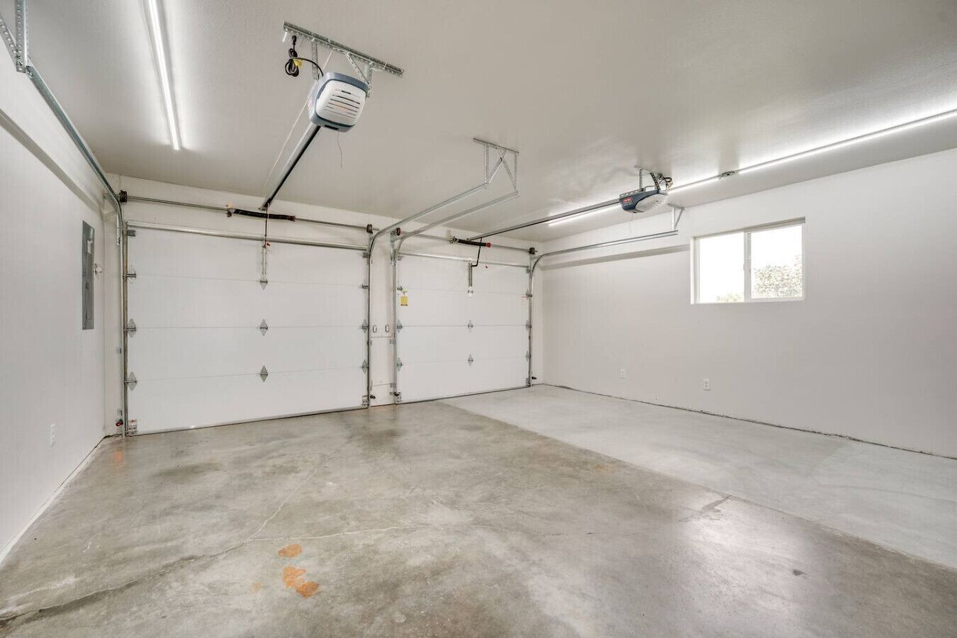 Un grand garage doté de quatre portes de garage blanches, d’un sol en béton et d’un éclairage fluorescent au plafond.