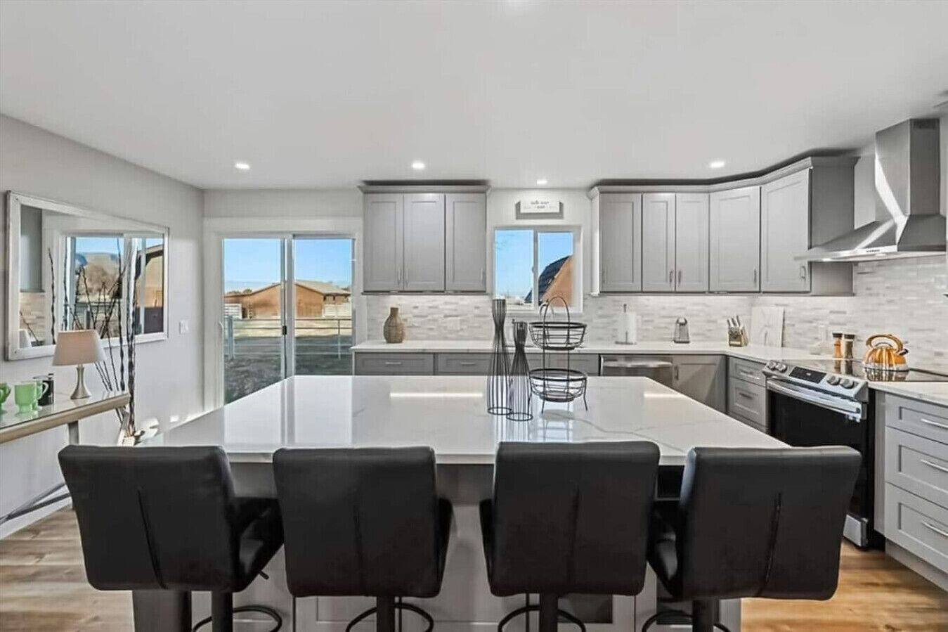 A modern kitchen with a large island, grey cabinets, and a view of the outdoors.
