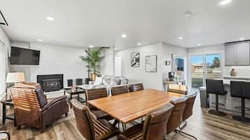 A modern dining area with a wooden table and leather chairs, a television, and a fireplace.