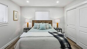 A bedroom with a bed, two bedside tables, two lamps, a headboard, a window with blinds, a door, and a wall-mounted picture. - 539 Massive 3 Bedroom Sleeps 10! (Yakima)