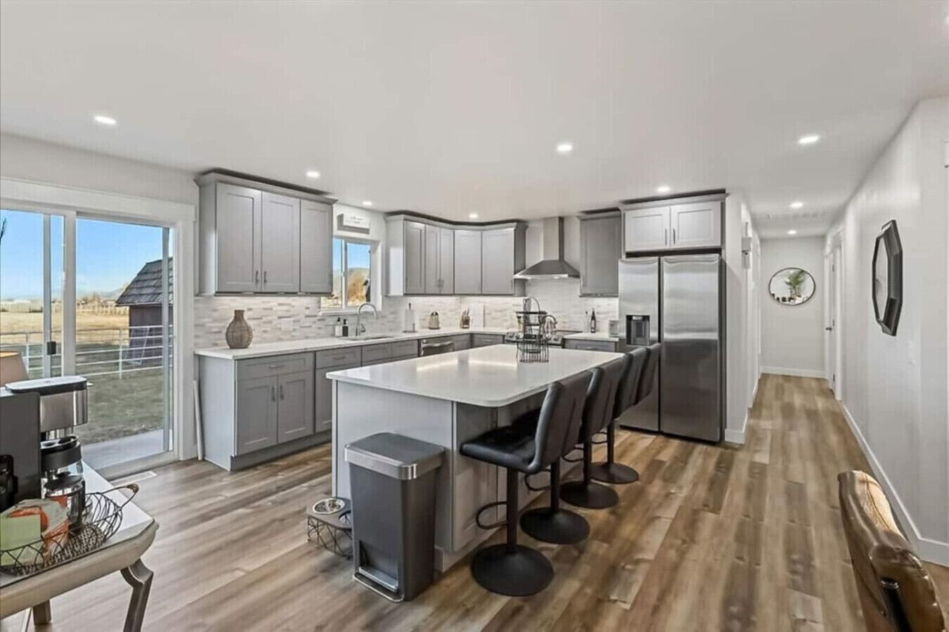 A modern kitchen with a large island, grey cabinets, stainless steel appliances, and a view of the outdoors.