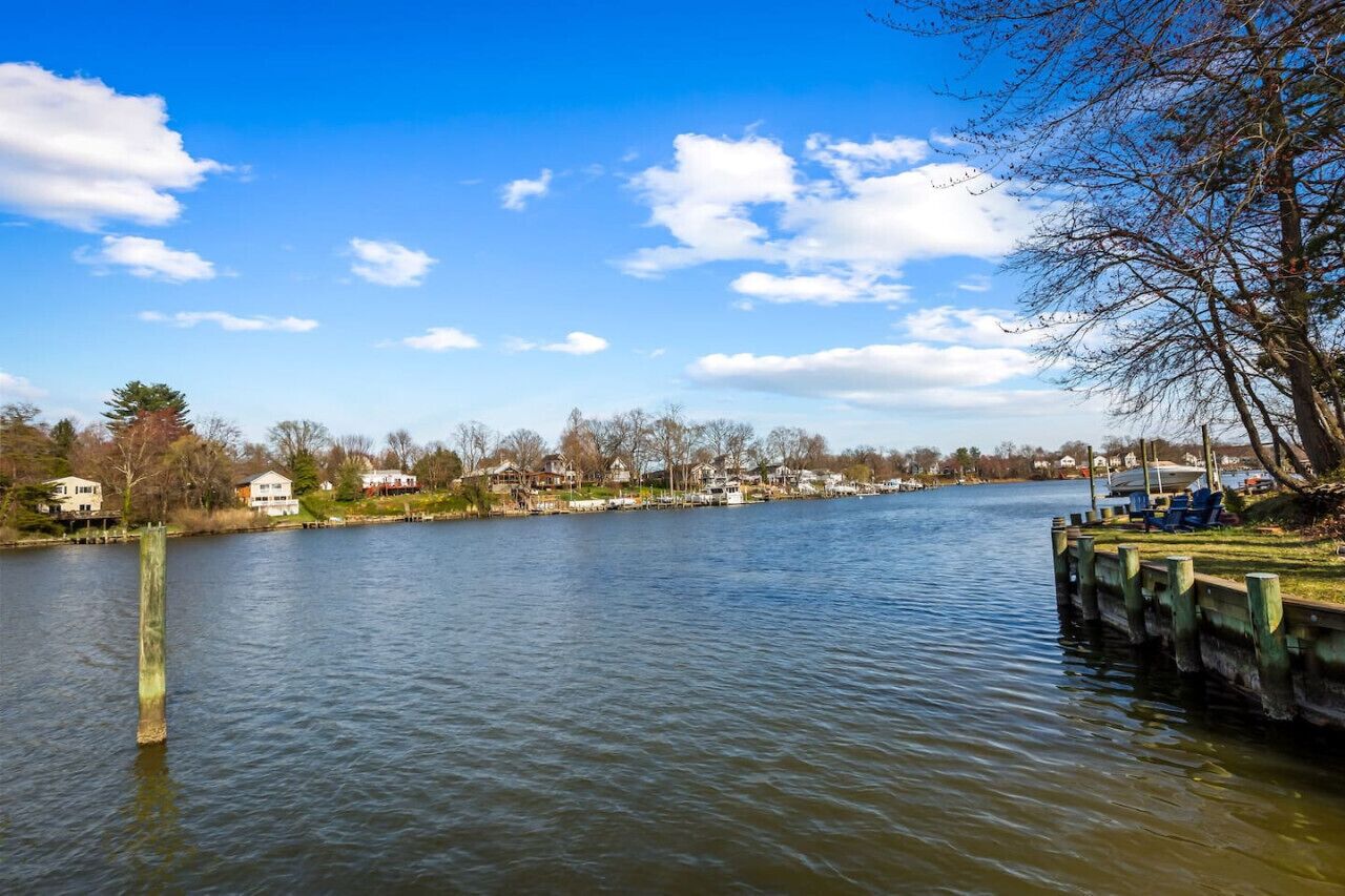 Une rivière bordée de maisons, un quai avec des chaises et un ciel dégagé.