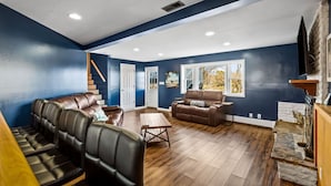 A spacious living room with a blue accent wall, a wooden staircase, leather seating, and a fireplace.