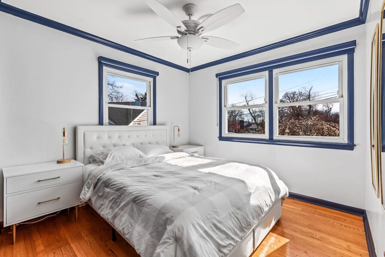 A bedroom with a bed, nightstands, a ceiling fan, and large windows.