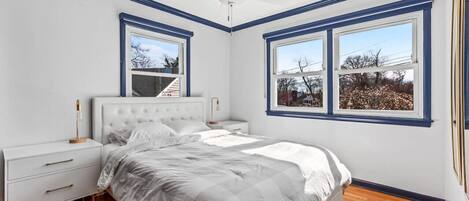 A bedroom with a bed, nightstands, a ceiling fan, and large windows.