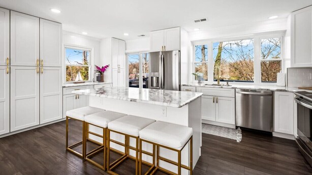 A modern kitchen with white cabinetry, a marble island, and a stainless steel refrigerator.