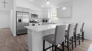A modern kitchen with white cabinetry, stainless steel appliances, and a central island with bar stools. - 561i Golf Cart Pool Access Garage Parking (Wildwood)