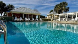 A clear swimming pool with lounge chairs and a covered area, surrounded by palm trees and a building with a sloped roof. - 561i Golf Cart Pool Access Garage Parking (Wildwood)