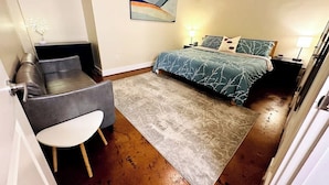 A bedroom with a bed, a chair, a small table, a rug, and a painting on the wall. - Ground-floor gem Walk to it all (Roanoke)