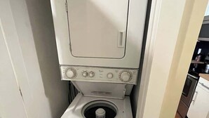 Eine kompakte Wascher und Trockner Kombination in einem kleinen Waschraum mit einer Tür zu einem Küchenbereich.