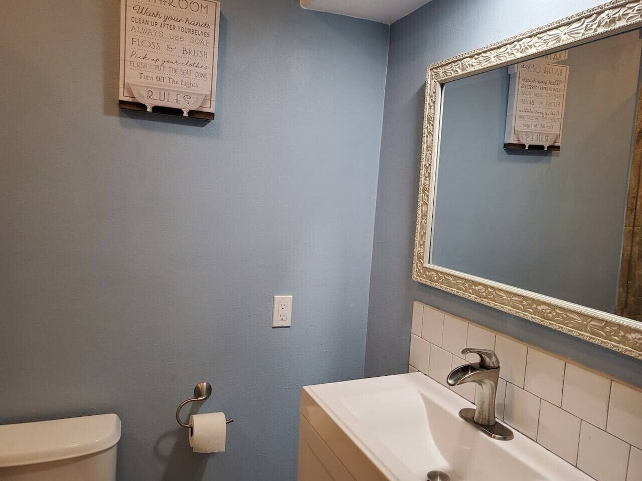 Ein Badezimmer mit Toilette, Waschbecken und Spiegel. An der Wand befindet sich ein Schild mit Reinigungshinweisen.