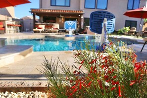 A swimming pool with a patio area, outdoor seating, and a building with a blue logo in the background. - 647 5 Bedrooms Hot Tub Firepit BBQ Kitchen (Glendale)