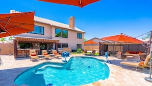 A swimming pool with lounge chairs and umbrellas, surrounded by a patio area with outdoor seating and a building in the background. - 647 5 Bedrooms Hot Tub Firepit BBQ Kitchen (Glendale)