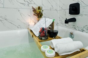 A bathroom with a marble wall, a wooden tray with a glass of red wine, a glass of water, a candle, and a bouquet of flowers. - 612 New Construction Fire Pit Games (Houston)