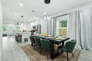 A modern kitchen with white cabinets, stainless steel appliances, and a dining area with a black table and green chairs. - 612 New Construction Fire Pit Games (Houston)