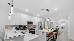 A modern kitchen with white cabinets, stainless steel appliances, and a central island with bar stools. - 612 New Construction Fire Pit Games (Houston)