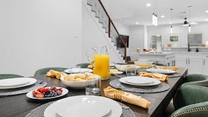 A modern dining area with a long table set for breakfast, including plates, glasses, and a pitcher of orange juice. - 612 New Construction Fire Pit Games (Houston)